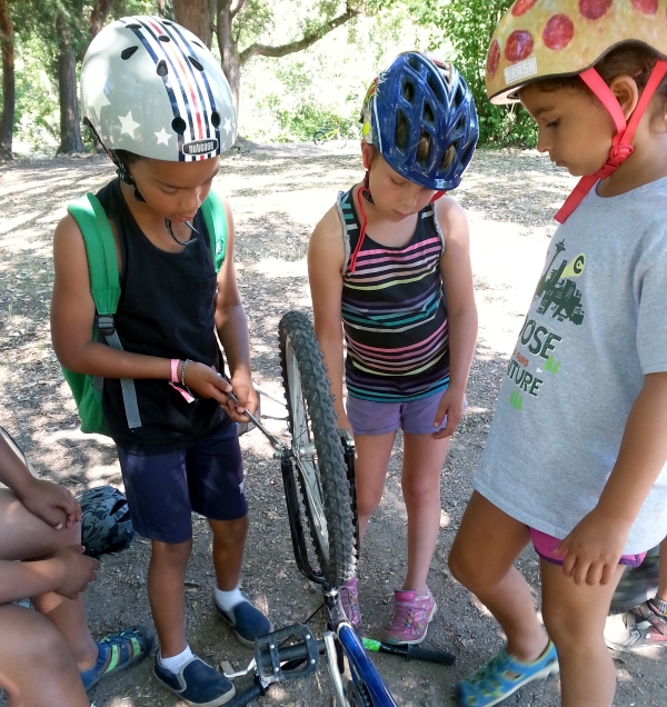 Three kids work together on fixing a bike wheel